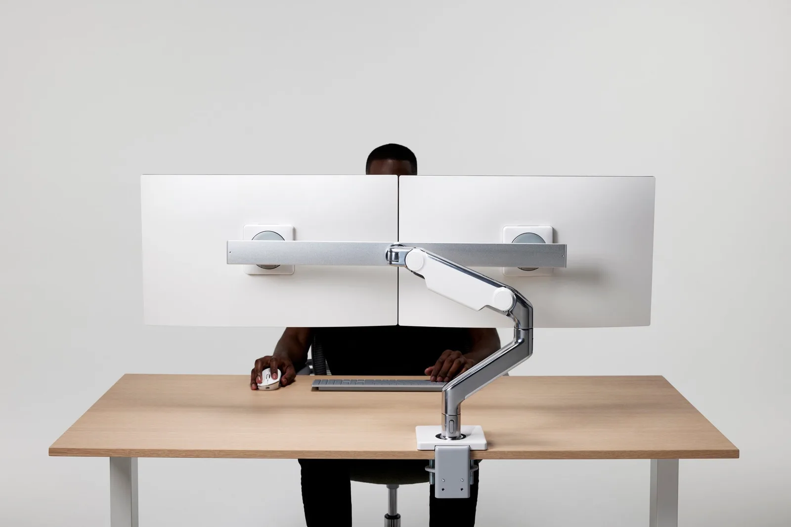 Dual monitor arm mounted on a desk, holding two monitors at eye level while someone types